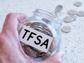 A hand holds a glass jar with a pile of coins and the words TFSA on it over a marble countertop.